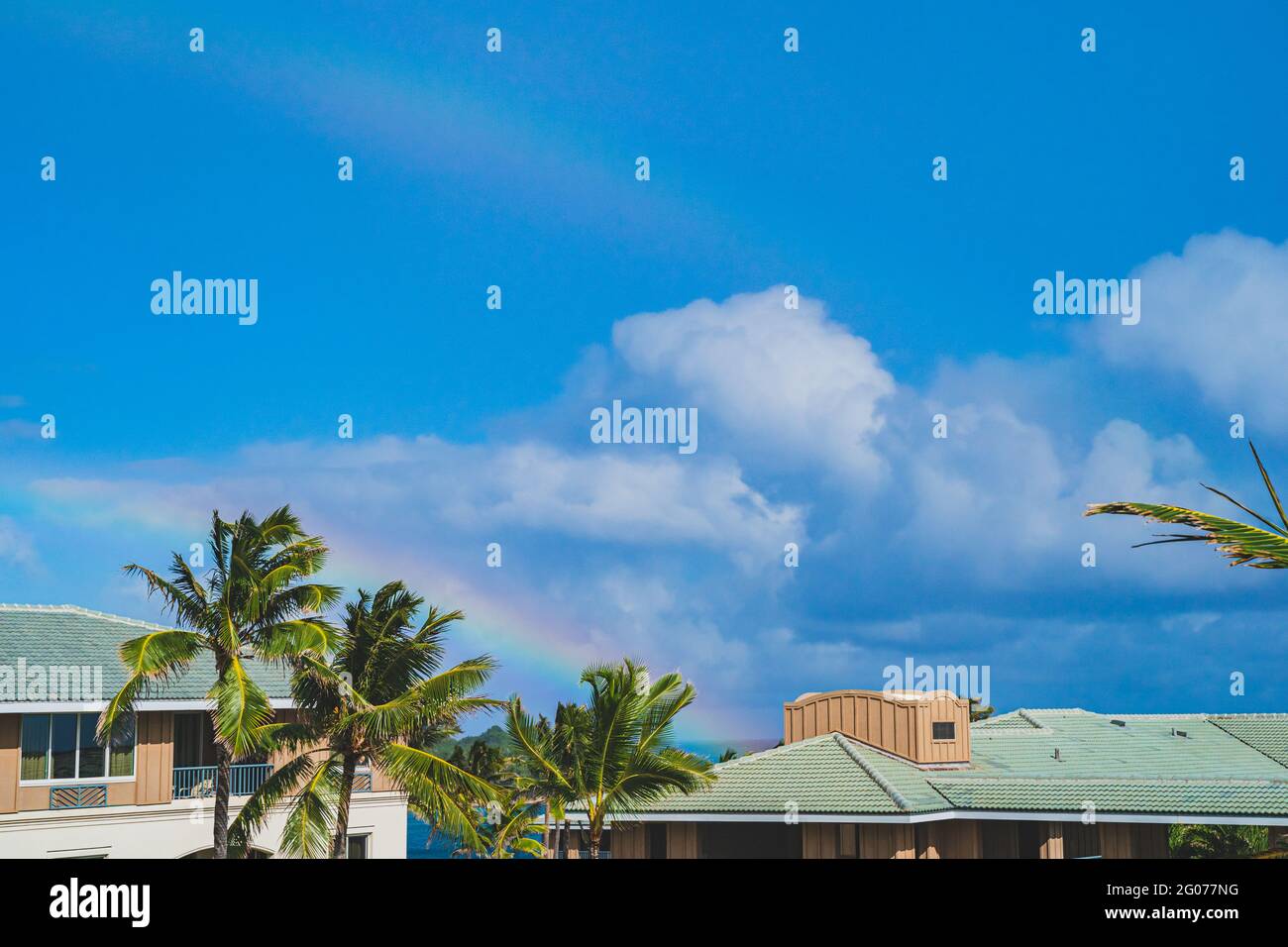 Double rainbow in blue sky above palm trees and rooftops in tropical paradise Stock Photo