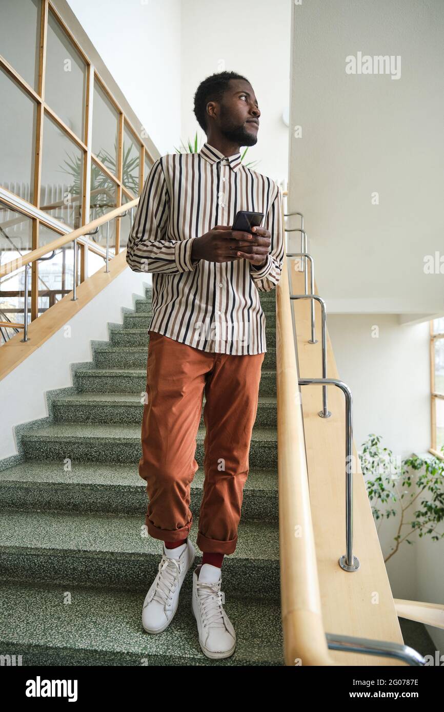 African young man using mobile phone while standing on stairs at office building Stock Photo