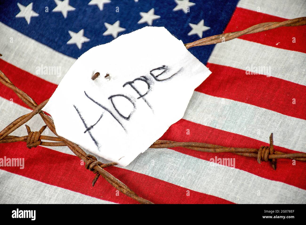 Hope text on torn white fabric on rusty barbed wire fence with American flag background Stock Photo