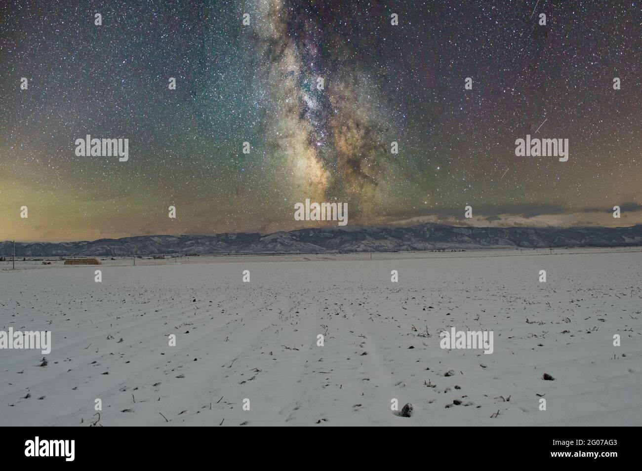 Milky way over a field covered with snow with mountains in background ...