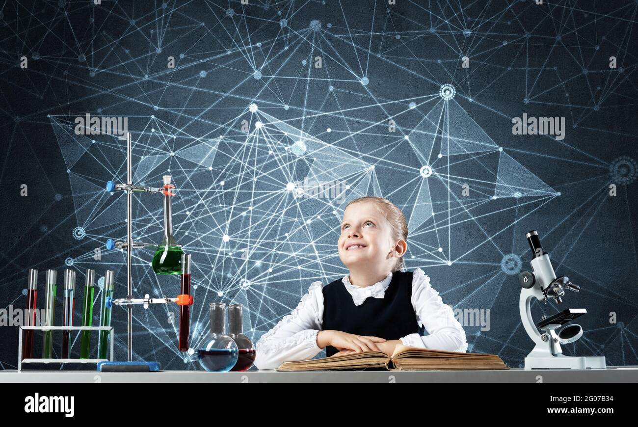 Smiling little girl sitting at desk with open book Stock Photo - Alamy