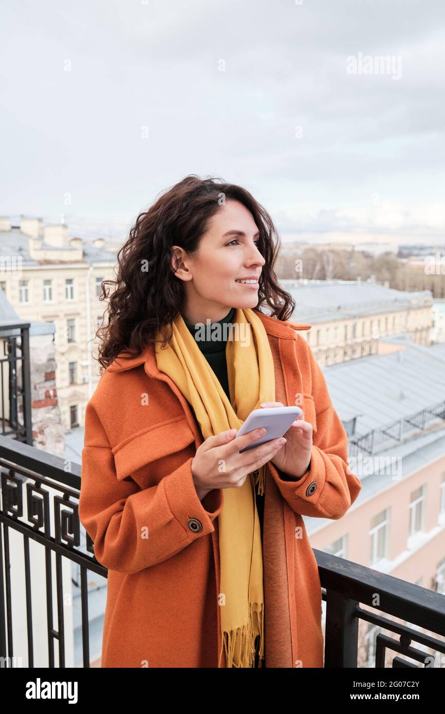 Young smiling woman using her mobile phone while standing outdoors Stock Photo