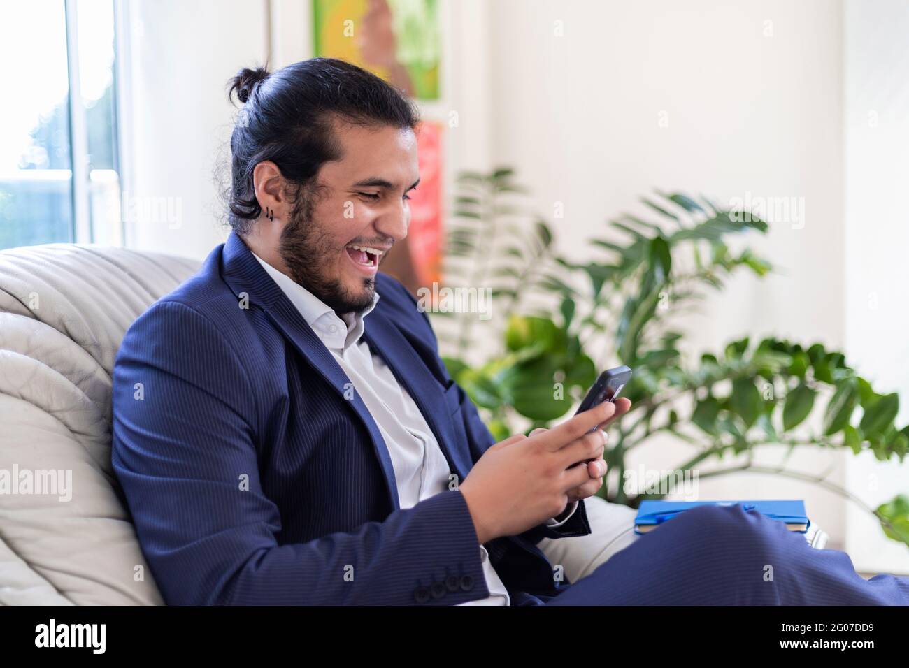 young latino man with long hair and piercings dressed in suit smiling while  texting on smart phone in home office. Home Office concept Stock Photo -  Alamy