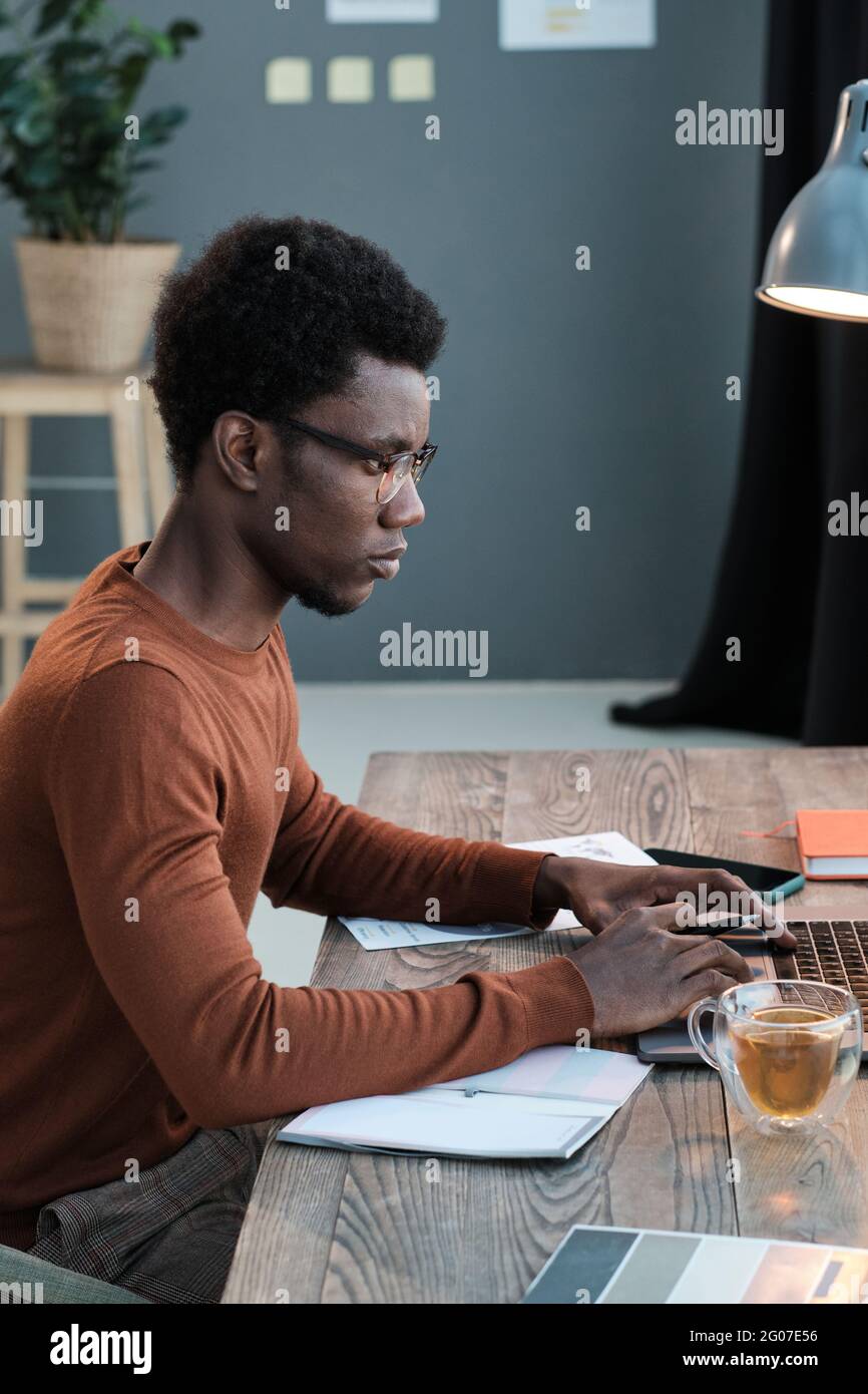 African young man sitting at the table and using computer for his study at home Stock Photo