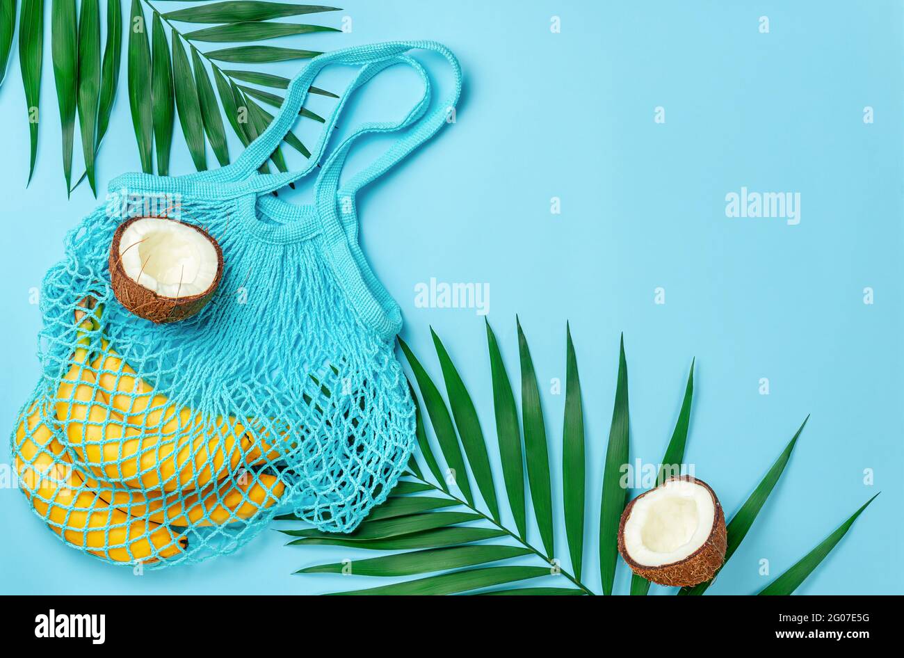 Zero waste mesh bag with bananas and coconut on bright blue background. Directly above, copy space. Stock Photo