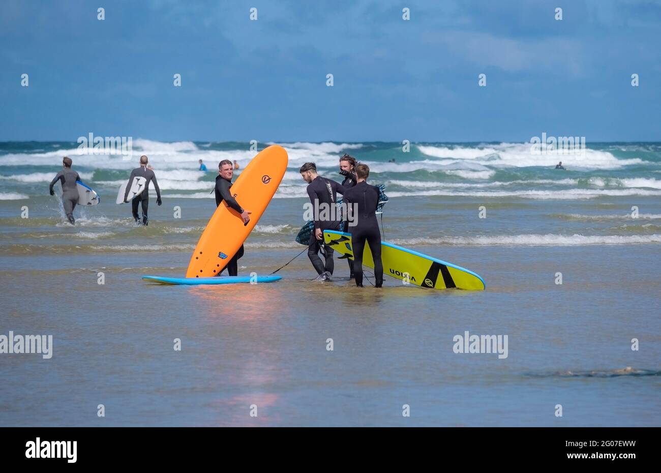 A group of friends carrying their hired surboards standing in the sea at Mawgan Porth on a Cornish staycation surfing holiday in the UK. Stock Photo