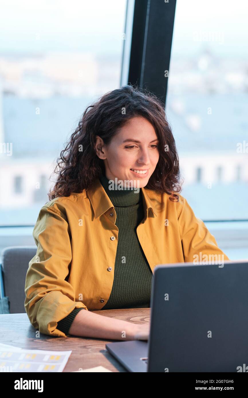 Young smiling woman sitting at the table and working on computer at office Stock Photo