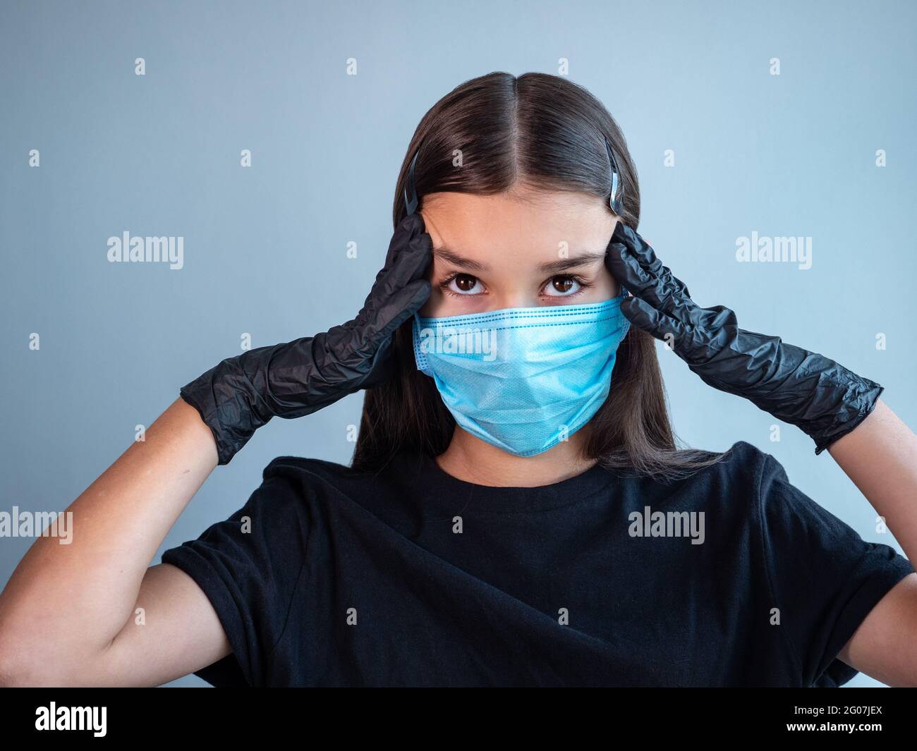 A female teenage girl in a blue protective medical face mask touching