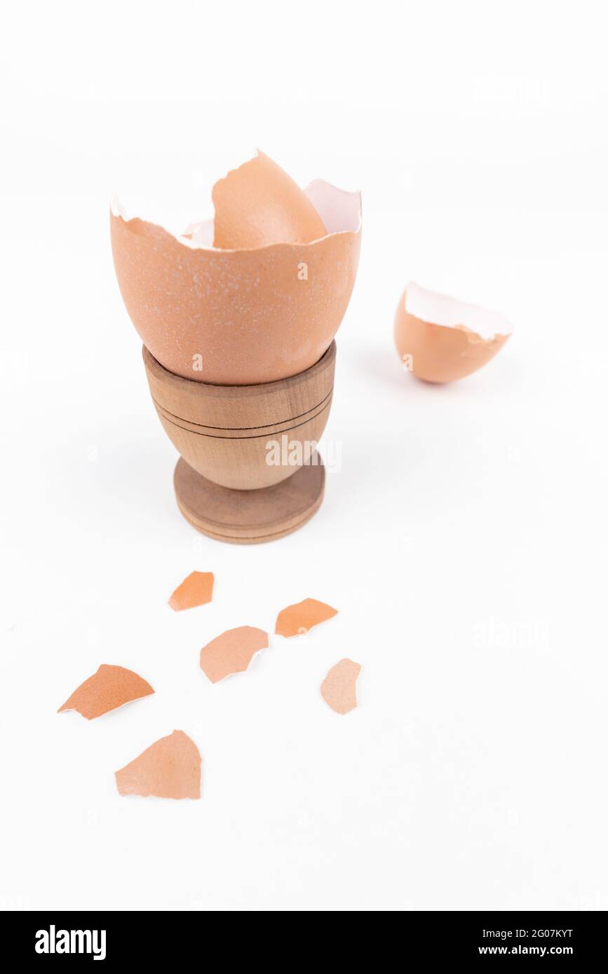 Broken egg shell in old wooden eg stand and scattered across white surface. Minimalism. Animal product concept. Simple breakfast. Sustainability issue Stock Photo