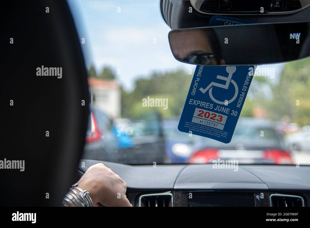 A plaque hanging from the rearview mirror of a car, showing a person inside the vehicle is disabled. Stock Photo