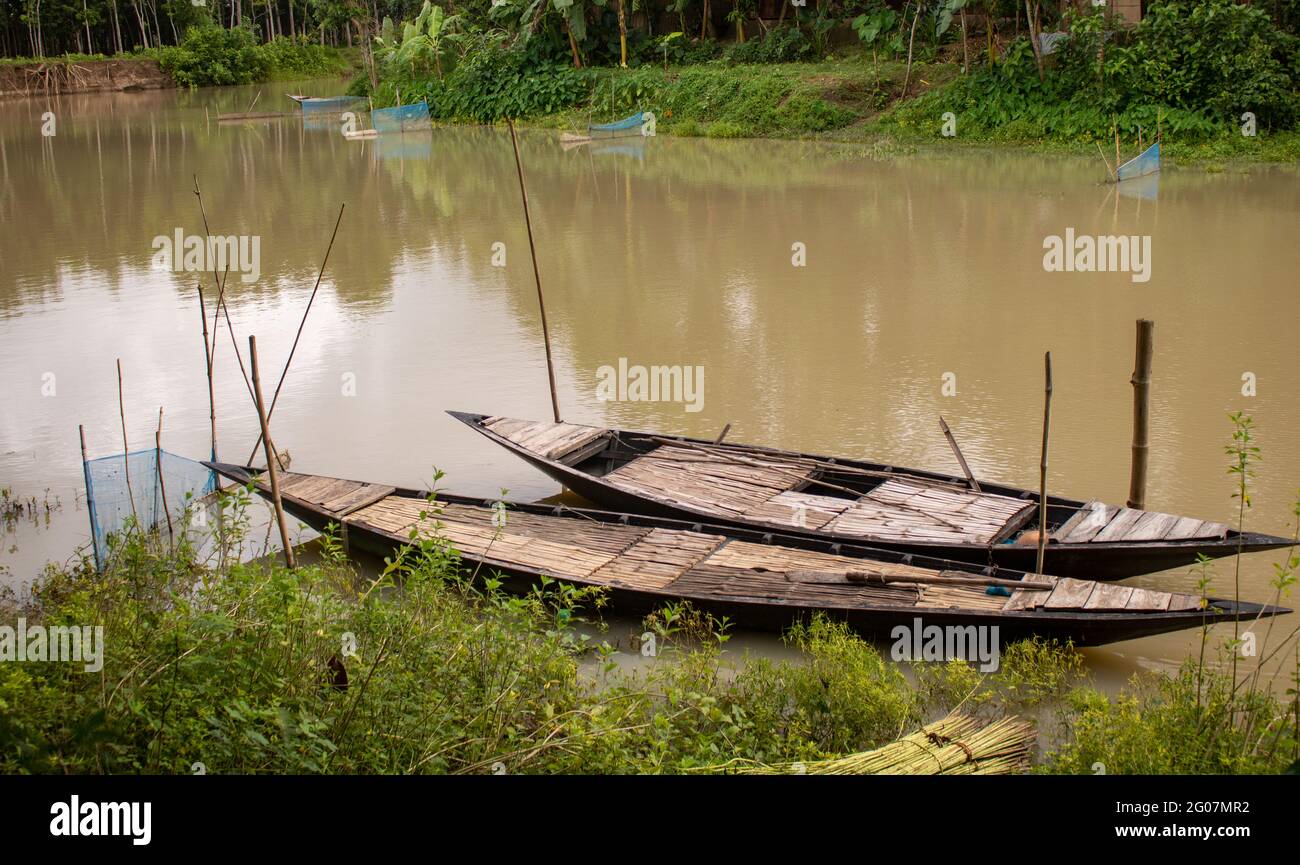 Bangladesh is a riverine country. A calm clear beautiful small river. There are two boats tied up at the wharf. Stock Photo