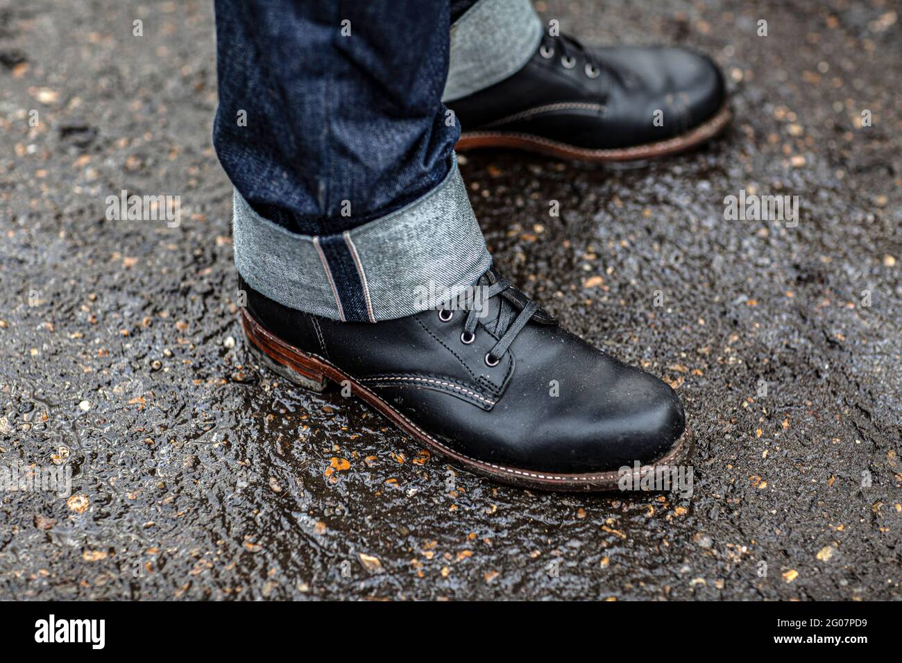 Close up shot of men in jeans and boots standing on wet street. rolling  your denim up Stock Photo - Alamy