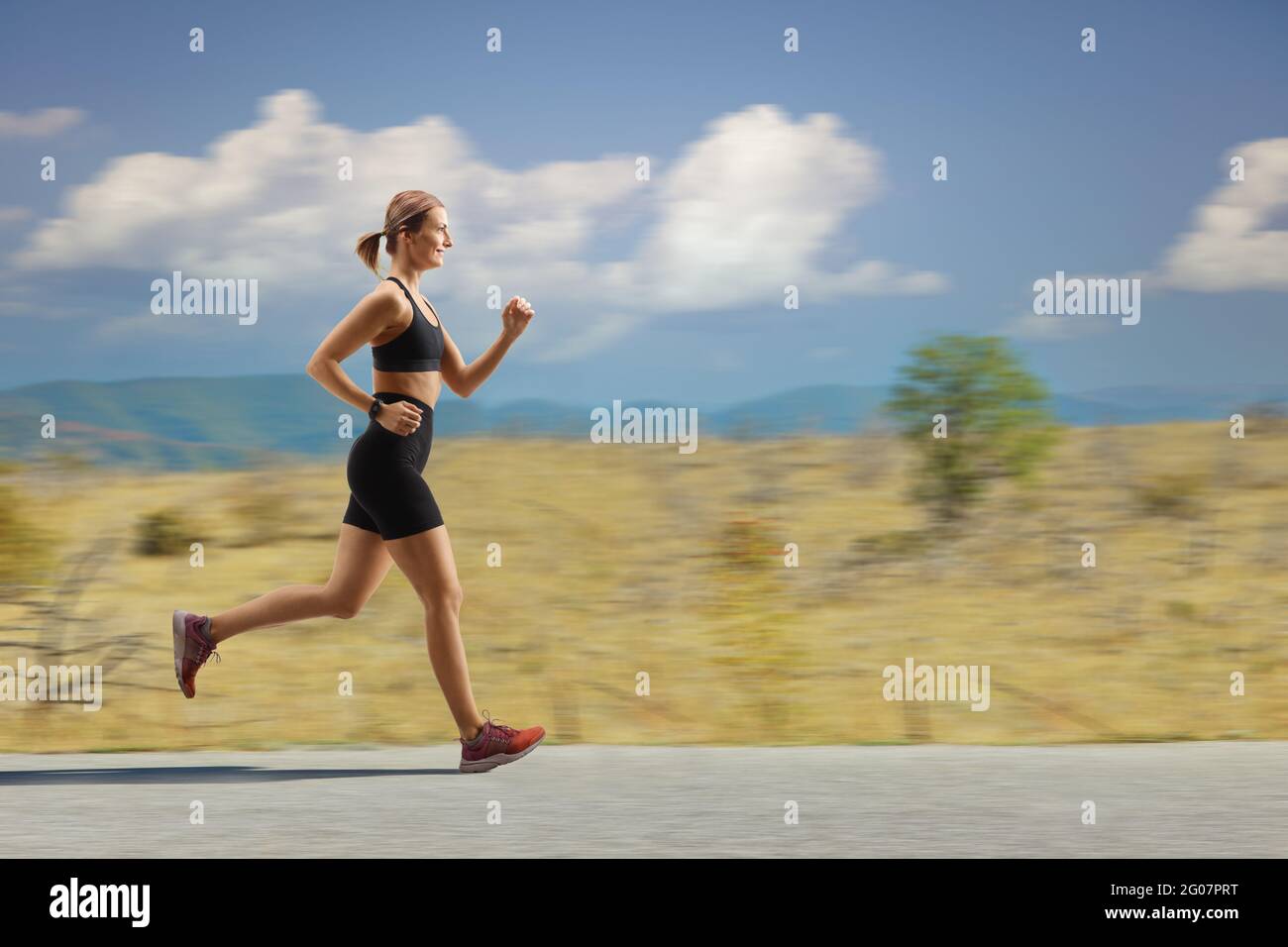 Full length profile shot of a fit young woman jogging on an open road Stock Photo