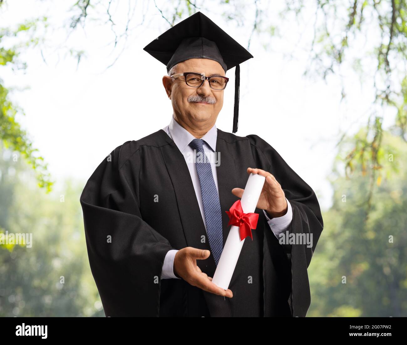 Mature man in a graduation gown holding a diploma outdoors with trees in  the background Stock Photo - Alamy
