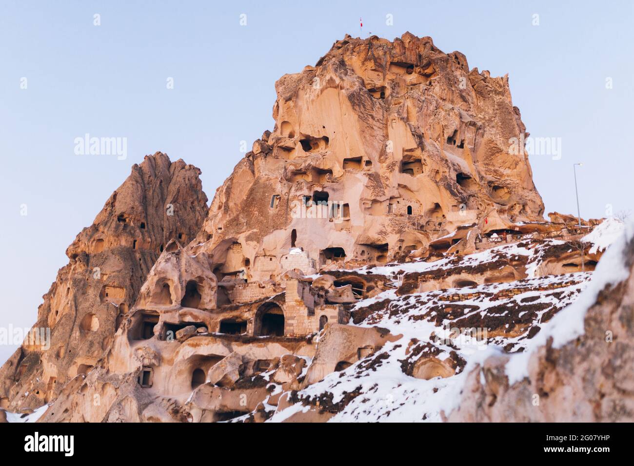 Low angle of aged castle carved in rock and covered with white snow against cloudless sky on street of Uchisar settlement in Cappadocia, Turkey Stock Photo