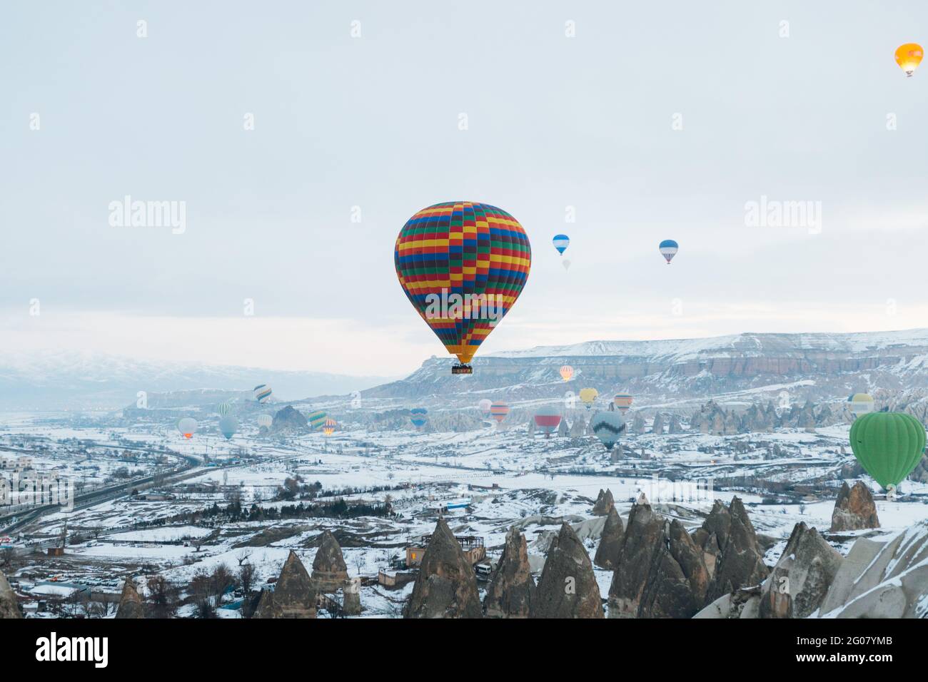 Multicolored air balloons n cloudy sky over ancient settlement with stone and cave houses against foggy highland in overcast weather in Turkey Stock Photo