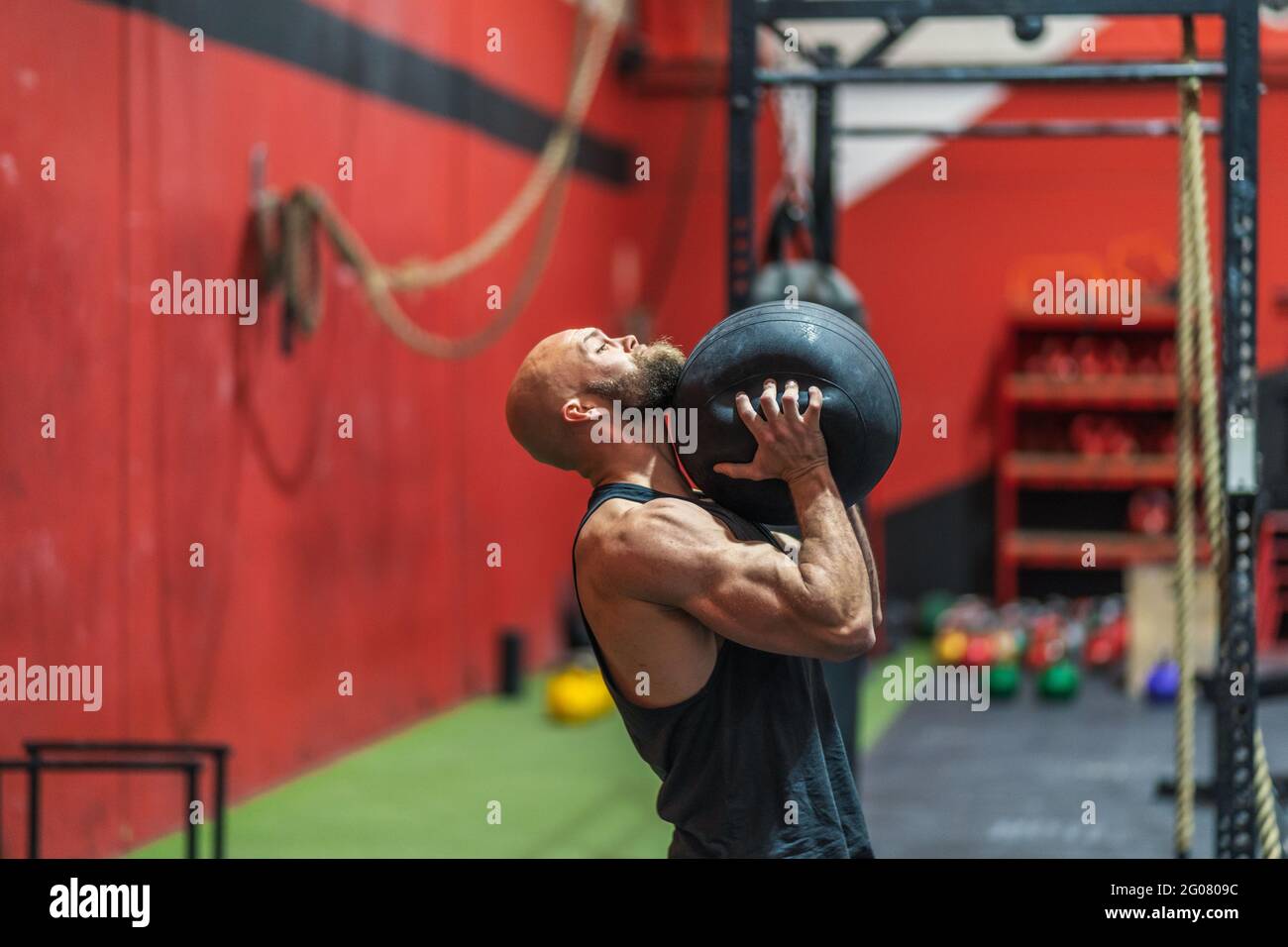 Side view strong male athlete lifting heavy ball while exercising