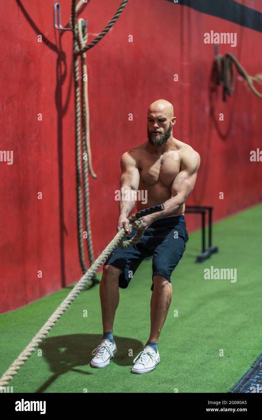 Strong sportsman pulling rope with heavy weights during intense workout