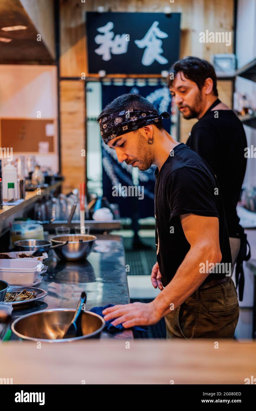 Side View Of Male Chef In Black Uniform And Bandana Cooking Asian Dish Called Ramen In Modern 