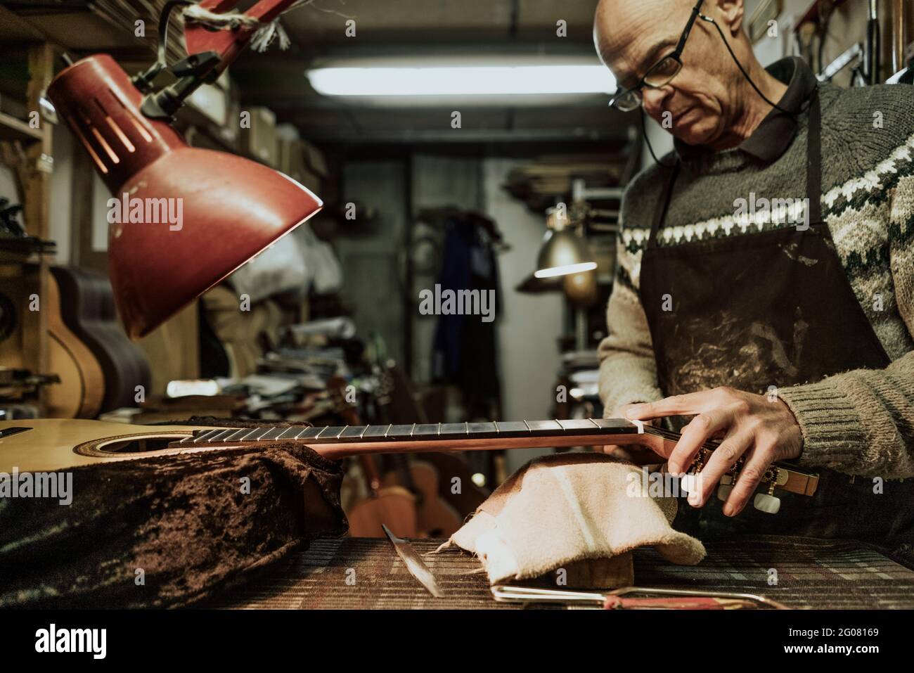 Mature male luthier in sweater measuring fret nut while repairing acoustic guitar at workshop Stock Photo