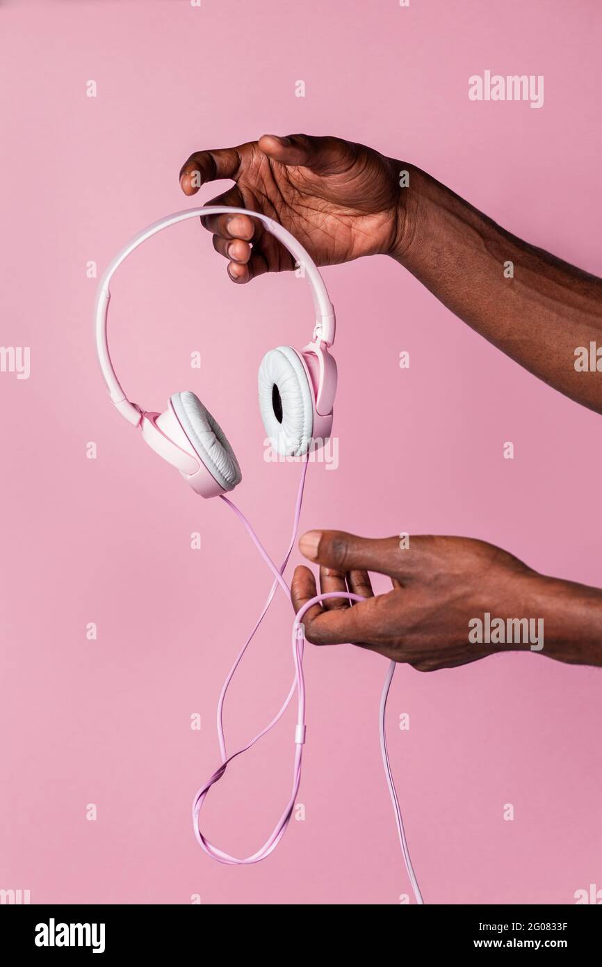 Hand of anonymous black man holding pink headphones against matching color background Stock Photo