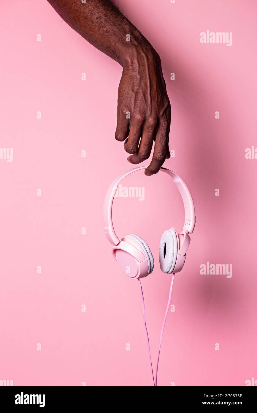 Hand of anonymous black man holding pink headphones against matching color background Stock Photo