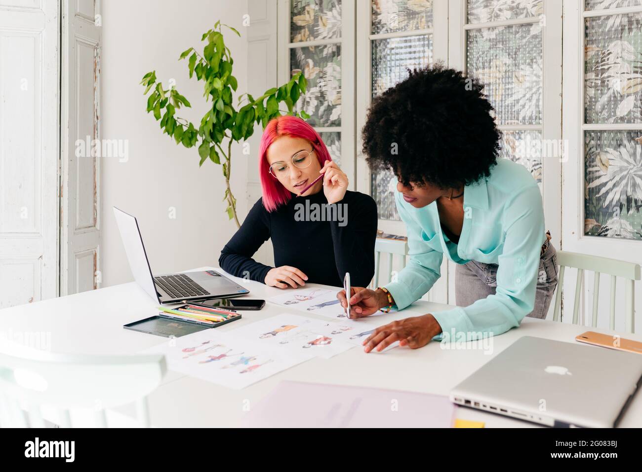 Young multiracial female fashion designers discussing sketches for new ...