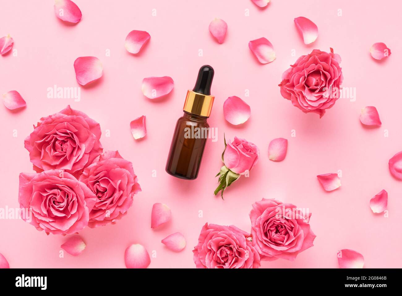 Brown glass dropper bottle for medical and cosmetic use and pink roses on a pink background. SPA concept. Top view, copy space for text Stock Photo