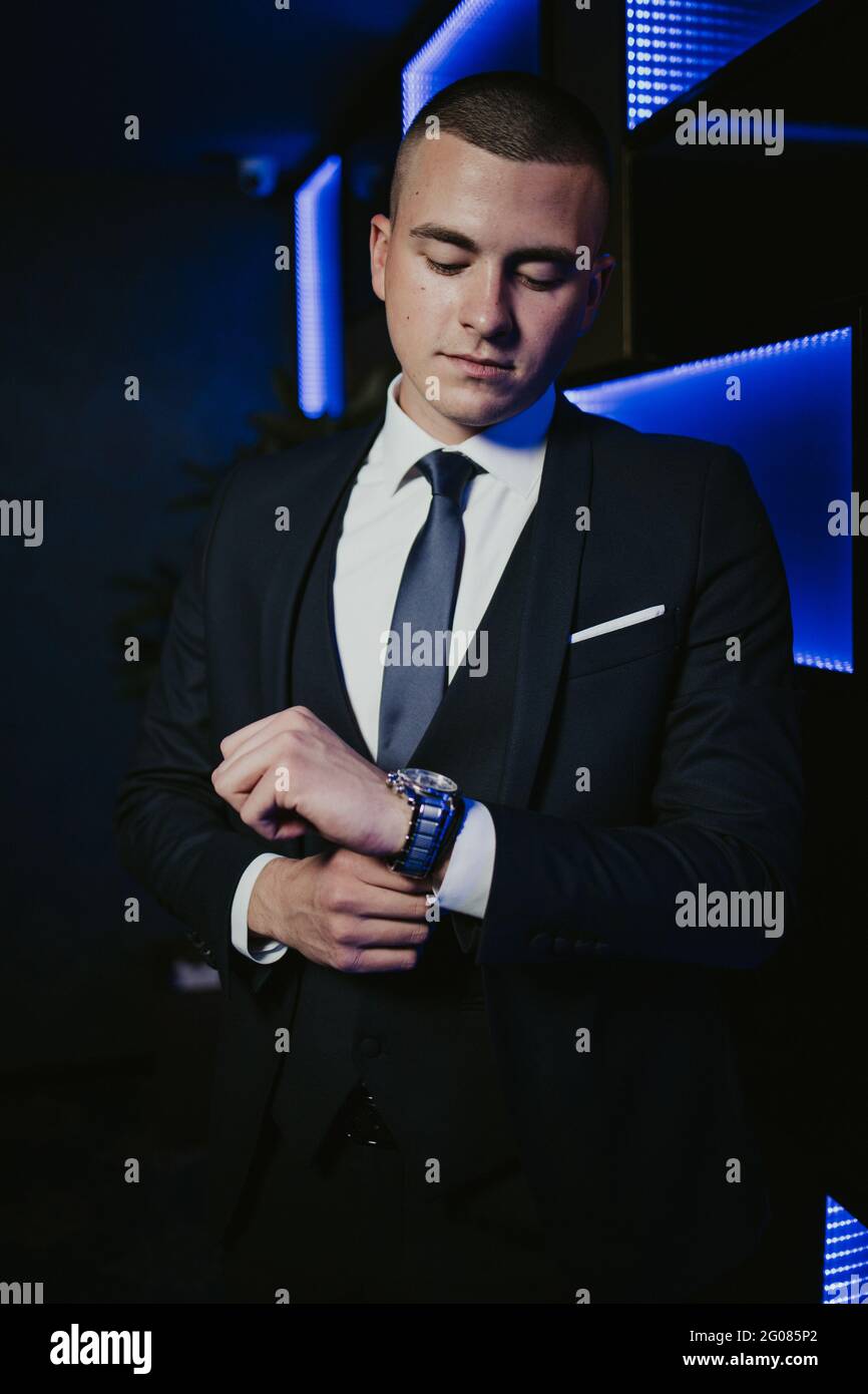 Vertical shot of a young caucasian man in a black suit checking the ...