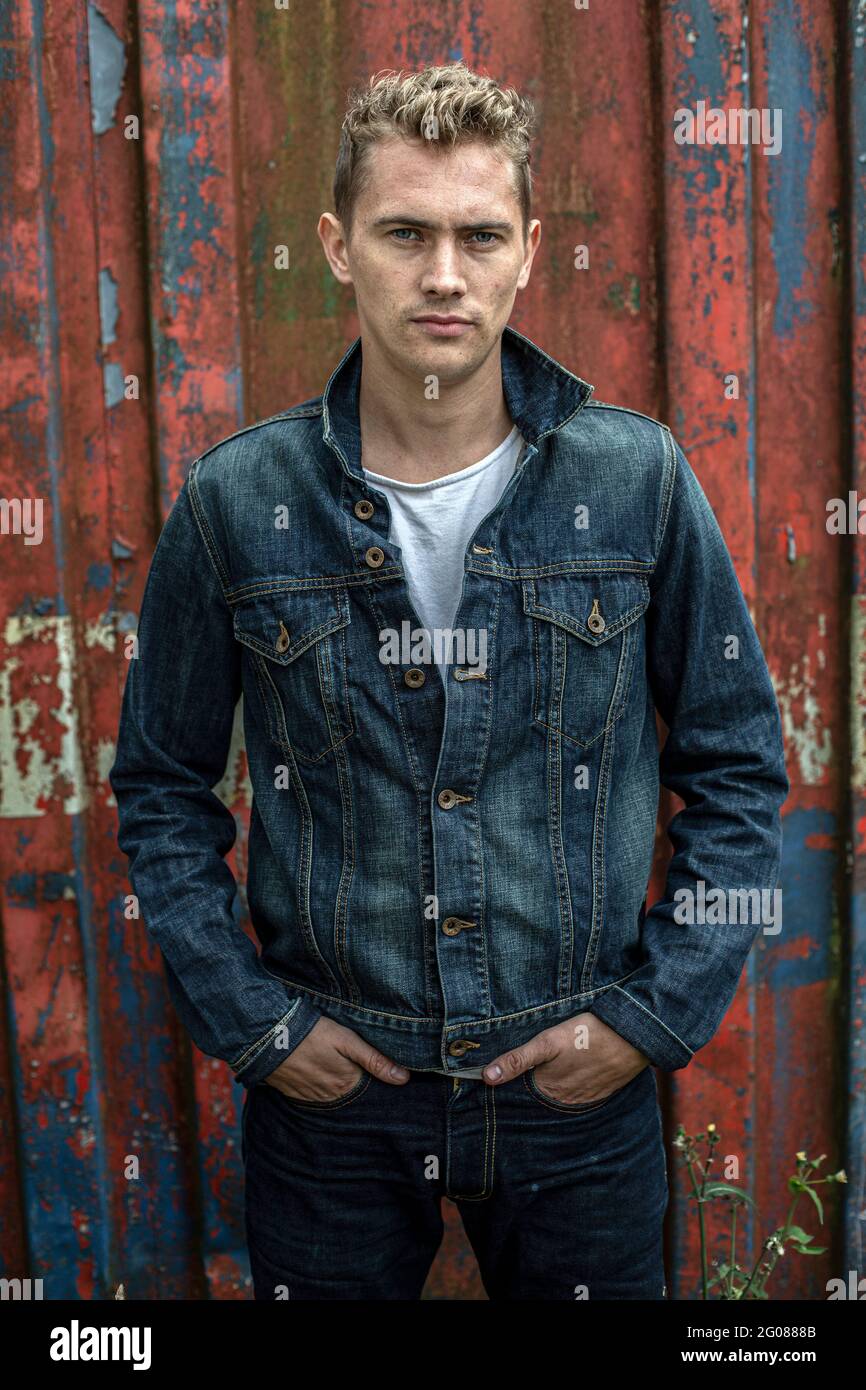 Handsome man wearing denim jacket with weathered red metal background Stock Photo