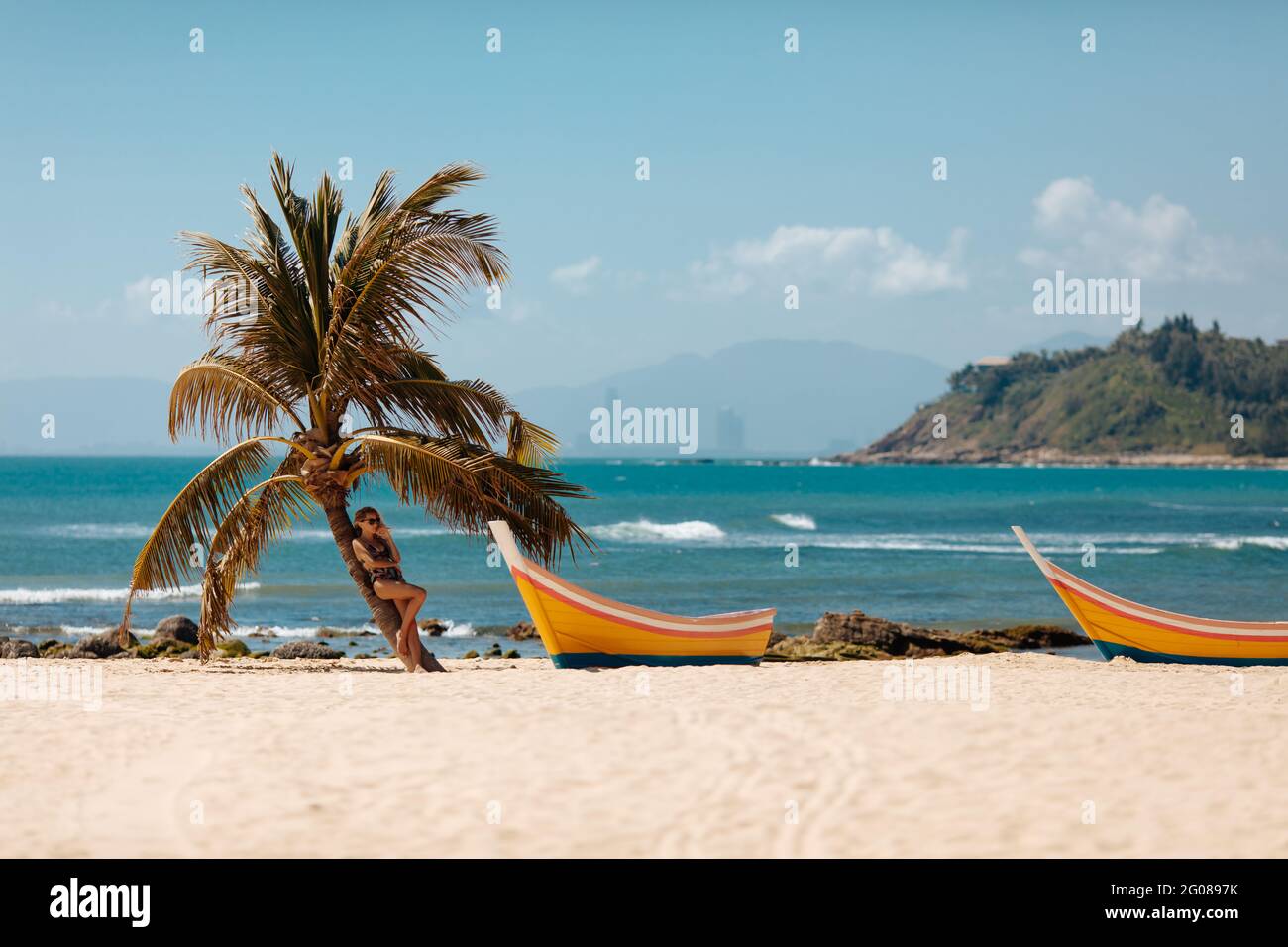 Beautiful woman in swimsuit relaxing near palm tree on beach Stock Photo