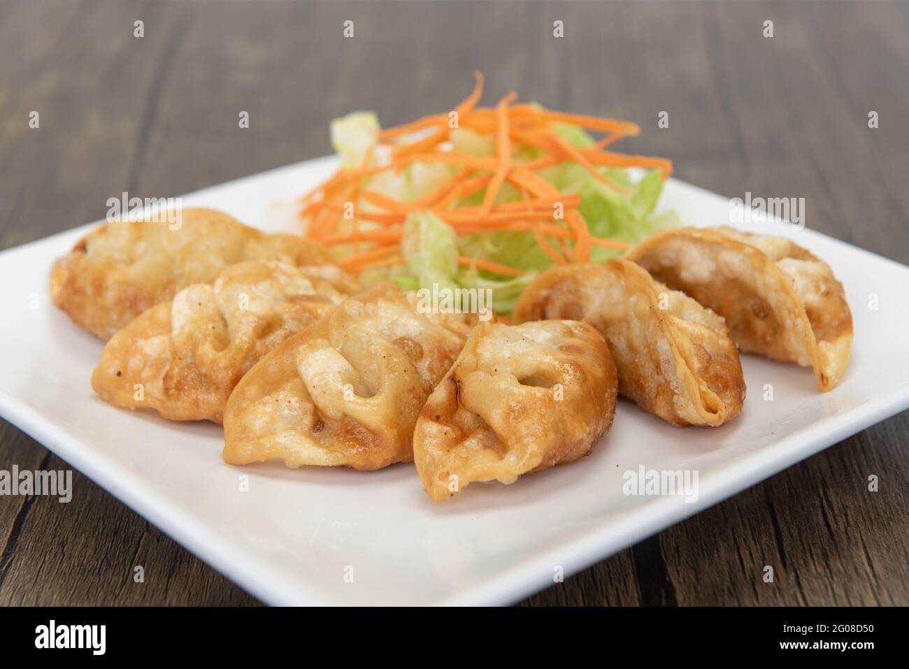 Deep fried gyoza arranged in an arc on a plate with garnishments for presentation. Stock Photo