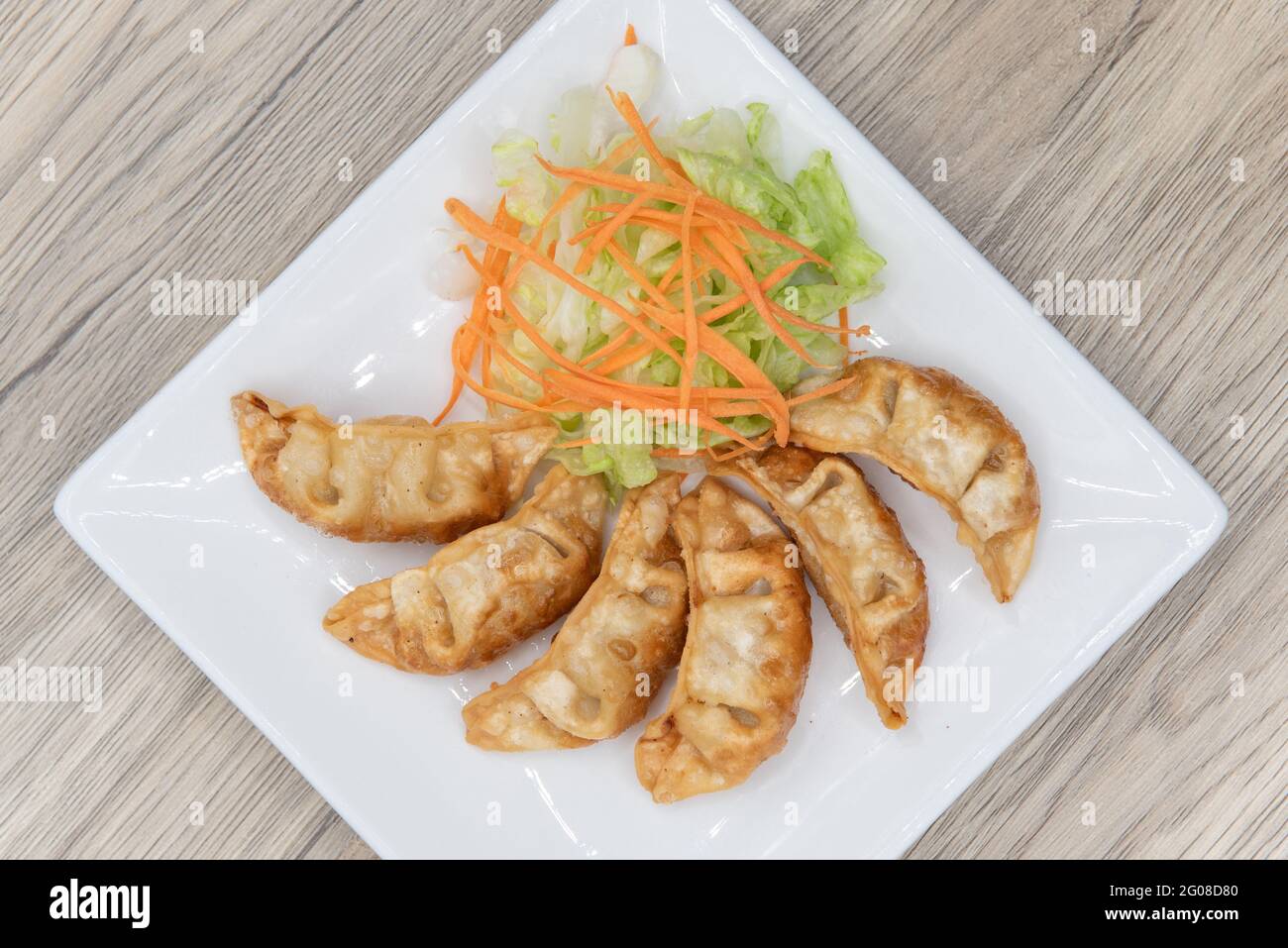 Overhead view of deep fried gyoza arranged in an arc on a plate with garnishments for presentation. Stock Photo