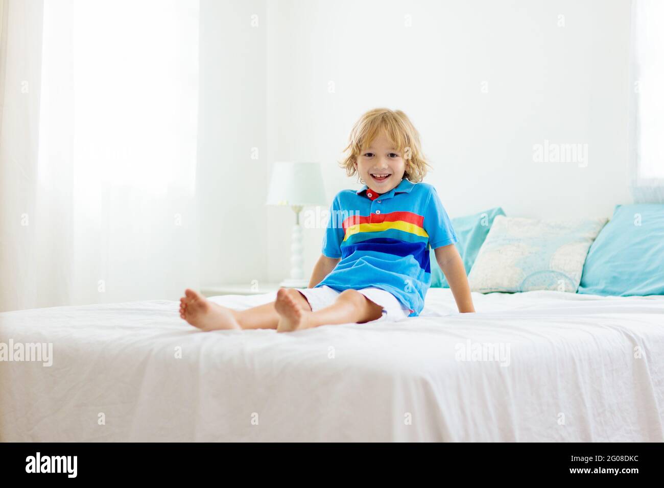 Child playing in bed in white sunny bedroom with window. Kids room and ...