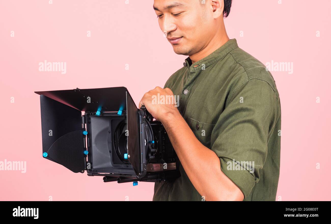 Portrait of Asian handsome young adult man confident professional videographer handheld holding digital video camera with matte box for cinema, studio Stock Photo