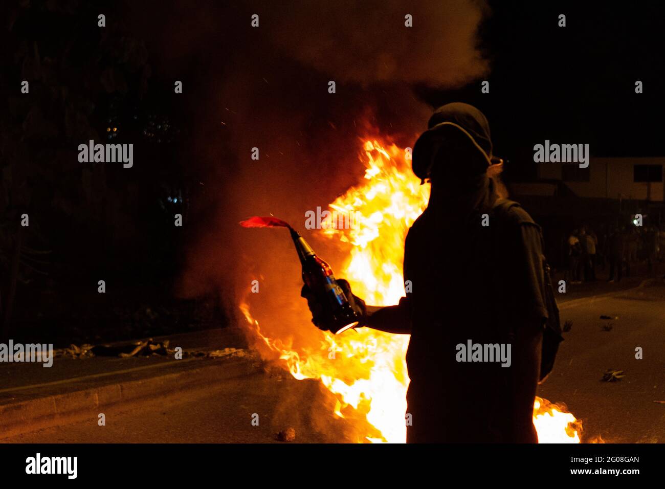 Medellin, Colombia on May 31, 2021. A demonstrator stands in front of a fire with a Molotov bomb as a group of hooded demonstrators clashes with Colombia's riot police (ESMAD) in Medellin, Colombia during the on going anti government protests against Presiden Ivan Duque's tax and health reform and police brutality and unrest that leaves at least 70 dead during the past month, in Medellin, Colombia on May 31, 2021. Stock Photo