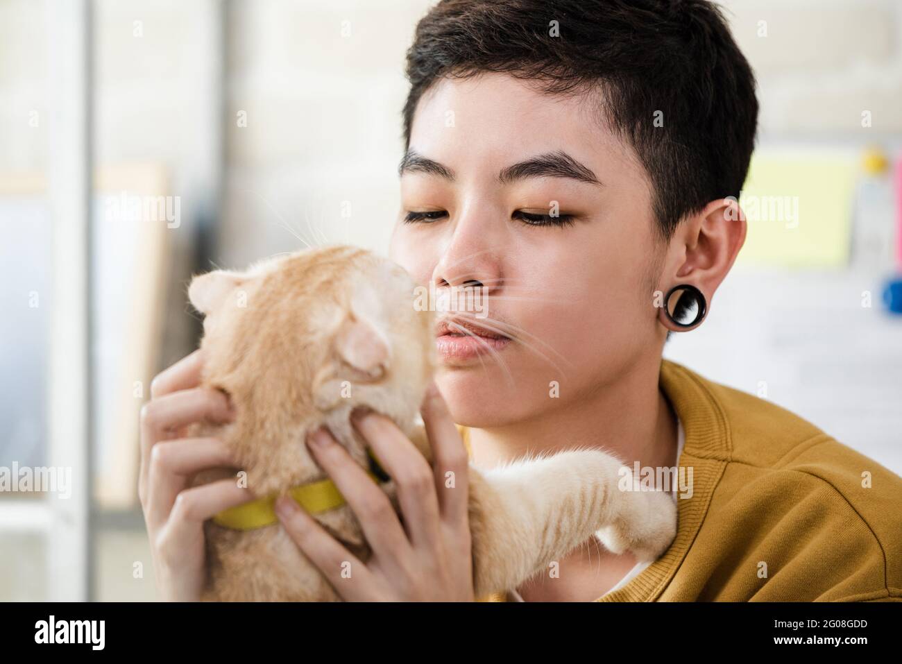 Close up shot of young Asian tomboy woman in casual attire holding and looking at her cat affectionately Stock Photo