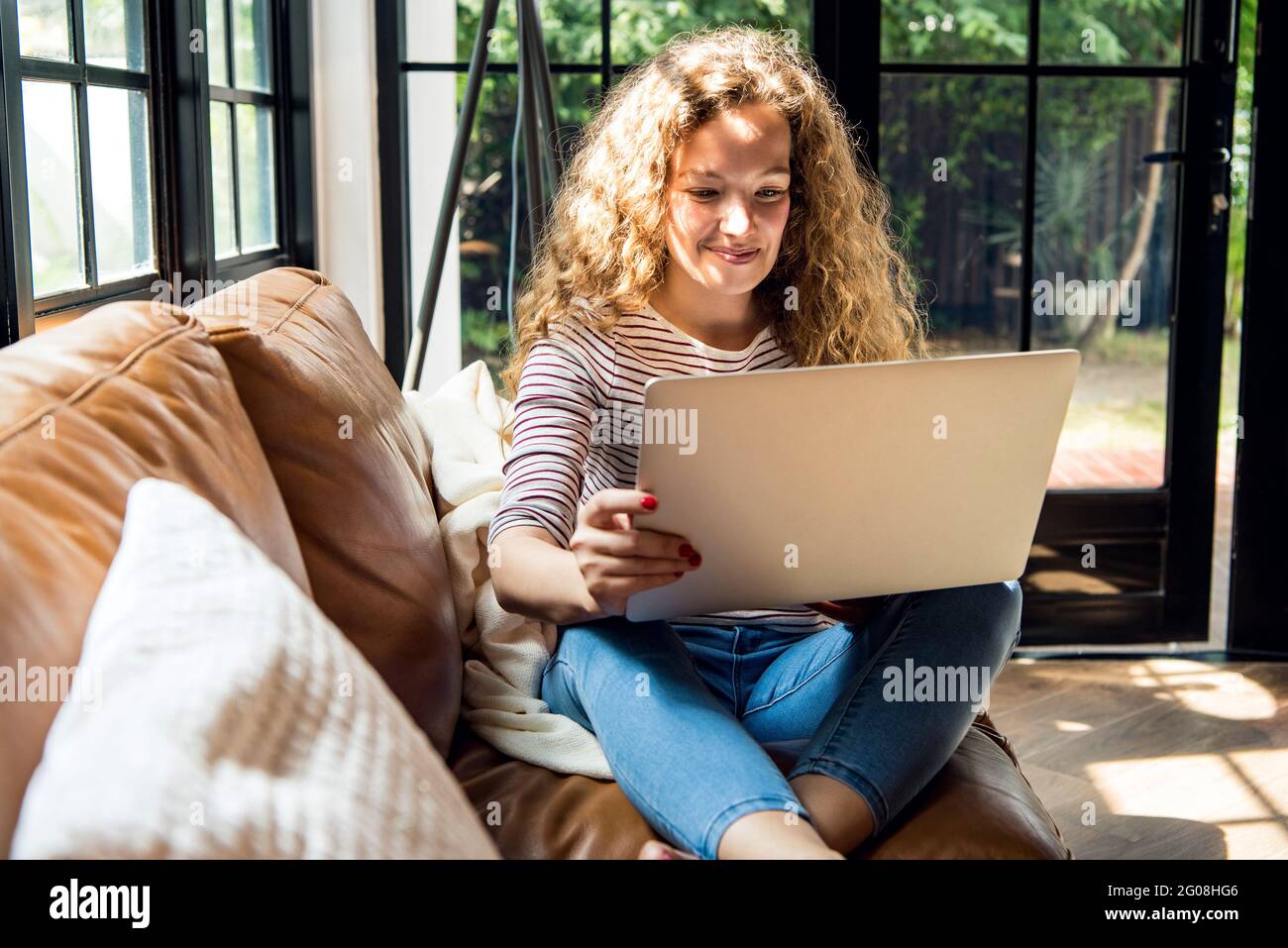 Pretty smiling Caucasian woman using laptop computer on the couch at home Stock Photo