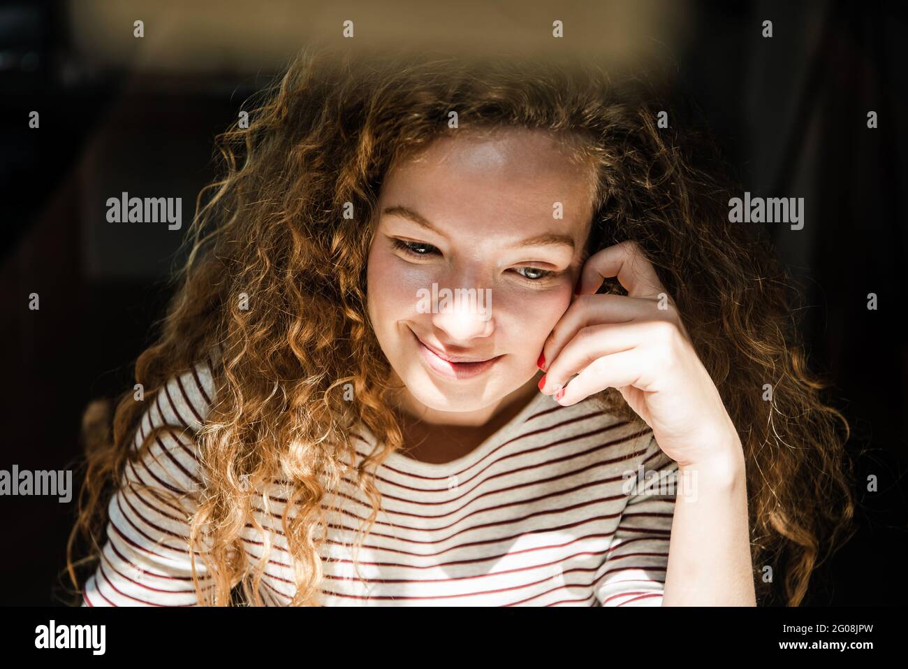 Young positive pretty Caucasian woman smiling and thinking with hand touching face in early morning Stock Photo