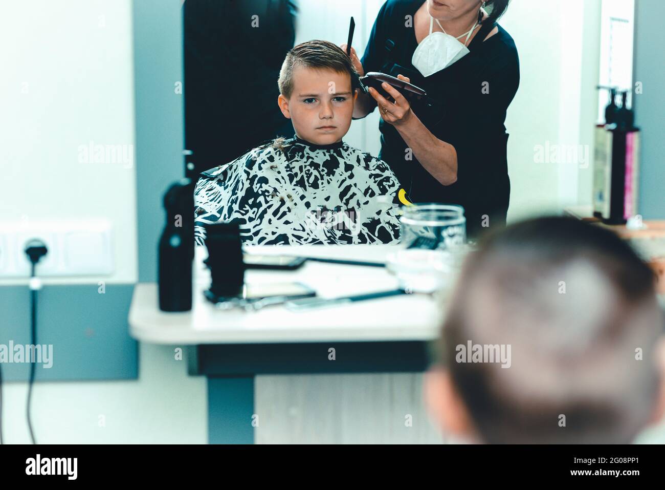 Cute kid boy have hair cut, professional barber doing haircut. Hairdress for children. Kid side view portraits in the barbershop.Toned. Stock Photo