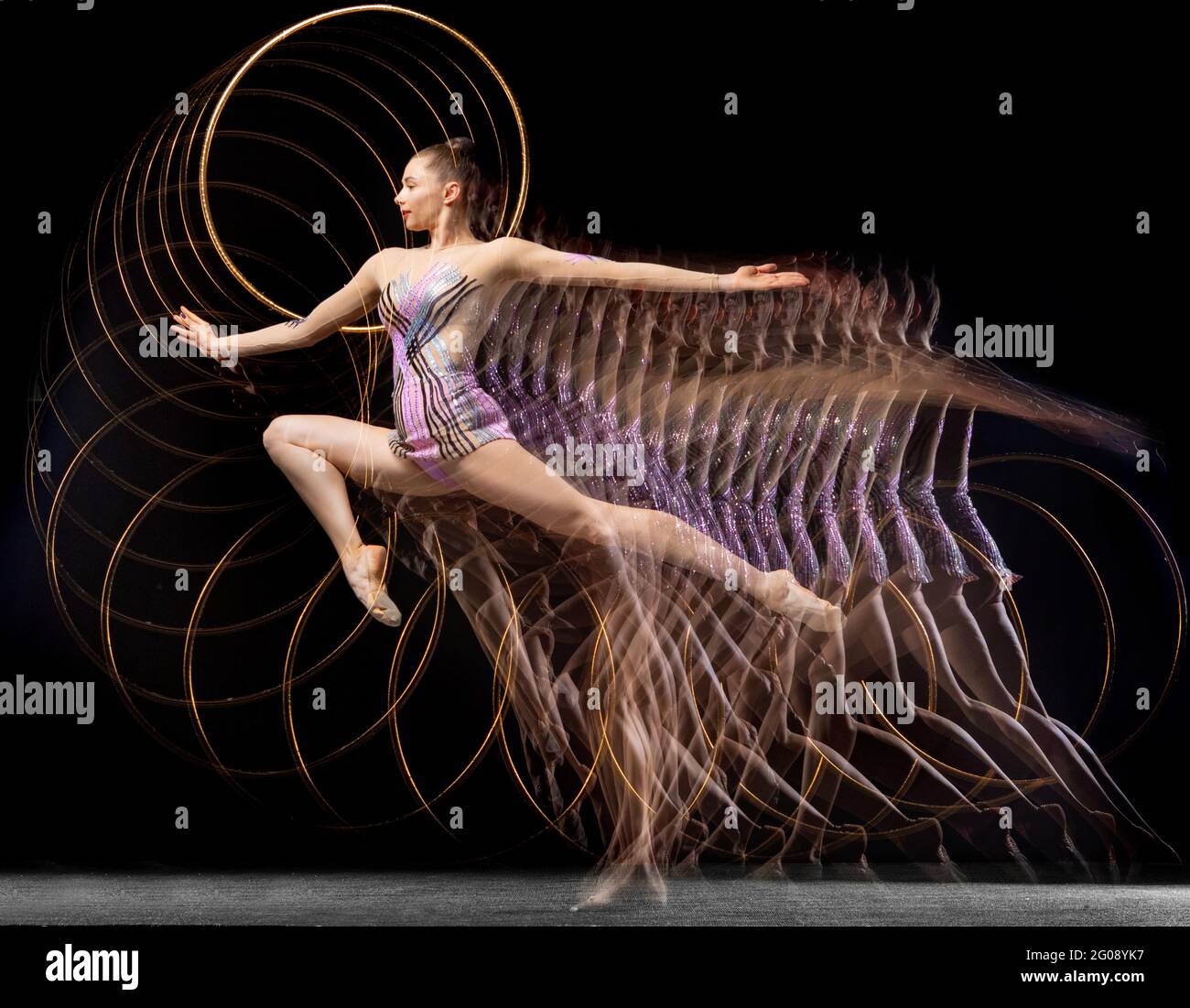 Portrait of young girl rhythmic gymnast in motion and action isolated in mixed light on dark background. Stock Photo