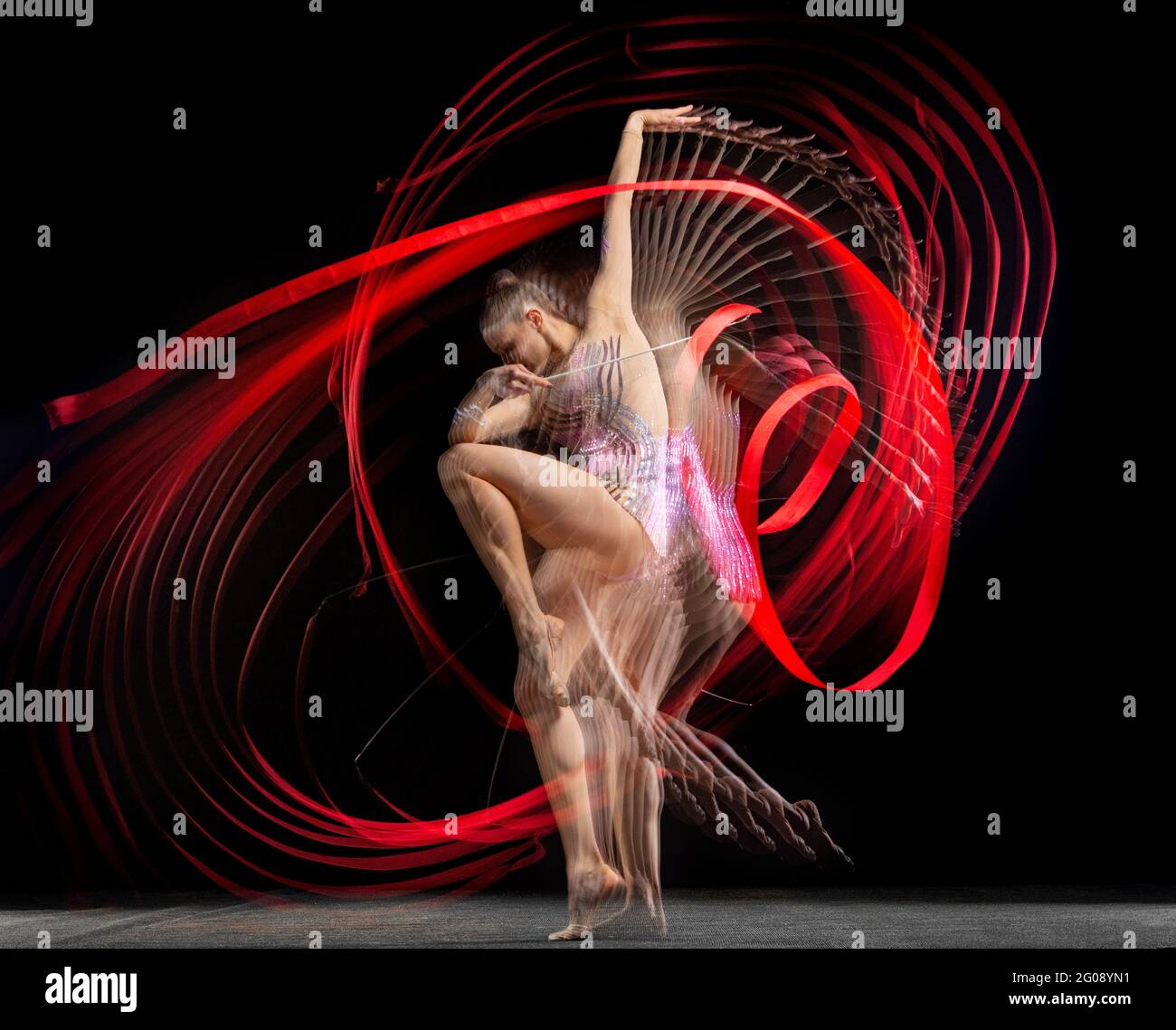 Young graceful girl rhythmic gymnast in motion isolated in mixed light on dark background. Stock Photo