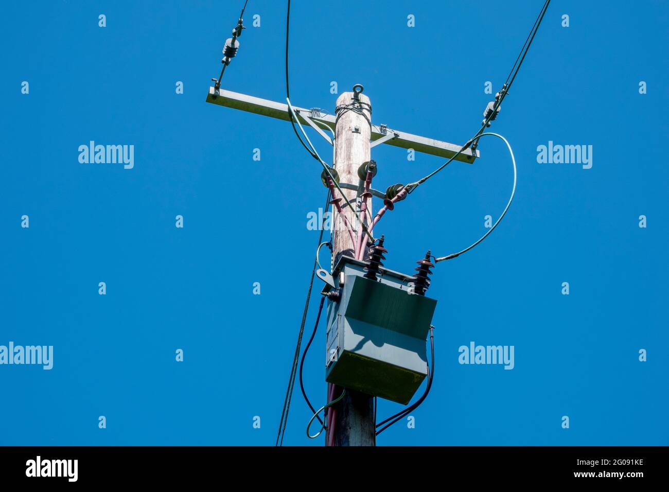 Transformer switch gear on top of a wooden pole carrying power against a blue sky Stock Photo