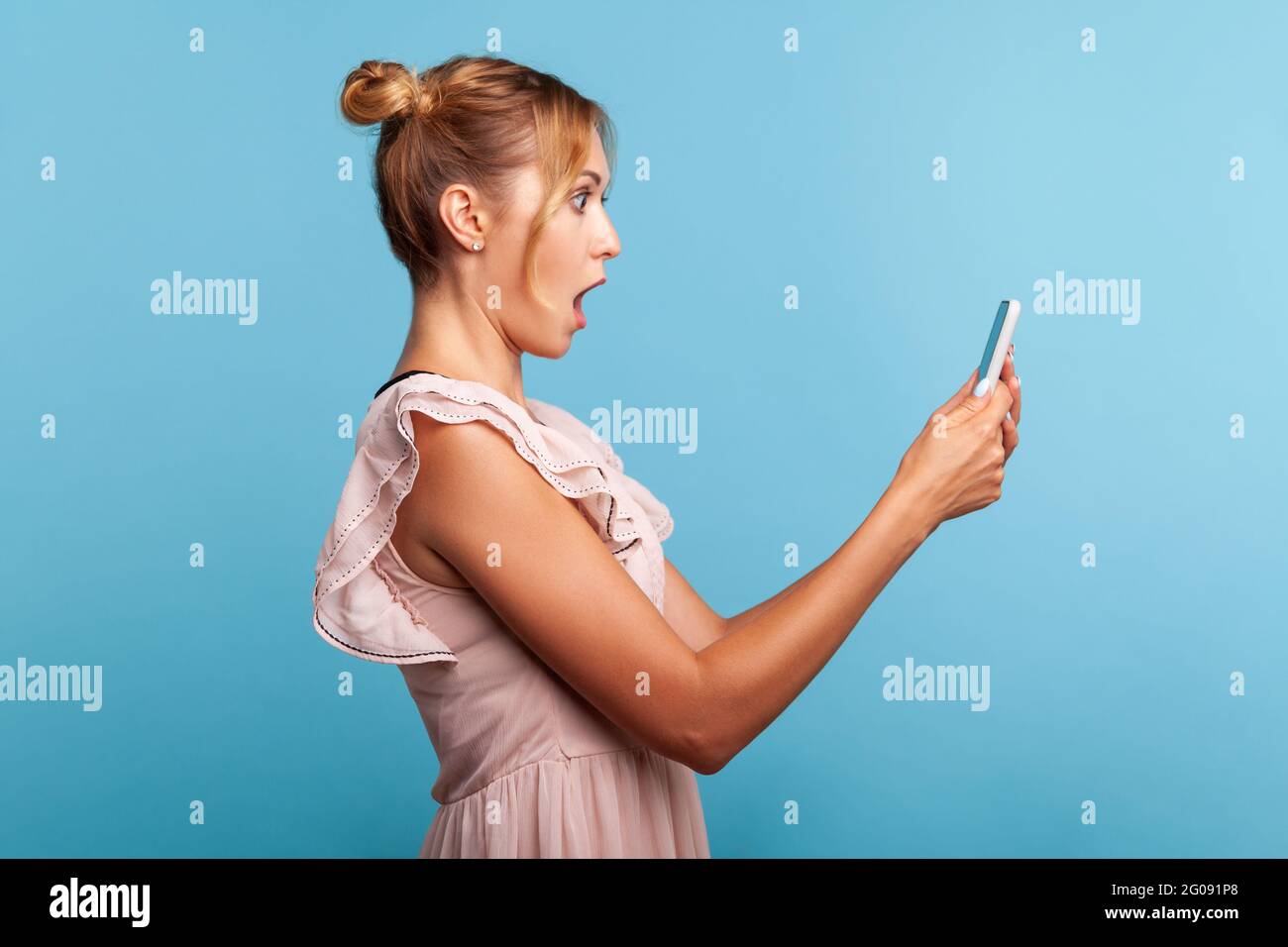Side view of surprised girl in stylish dress, expressing shock while using cell phone, online mobile application, searching web, astonishing news. Ind Stock Photo