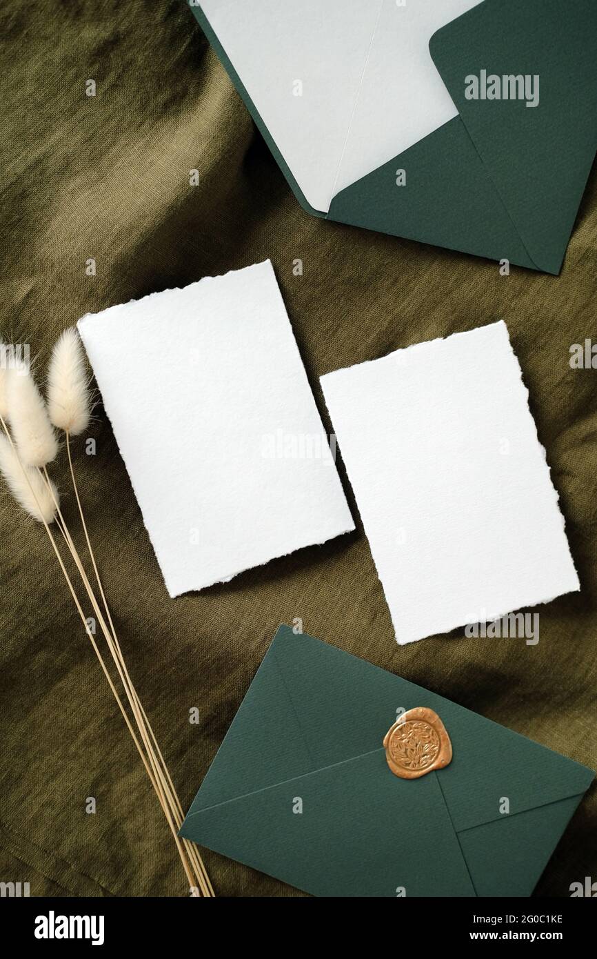Elegant wedding invitation cards and envelopes on green fabric with dried flowers. Flay lay, top view, copy space. Stock Photo