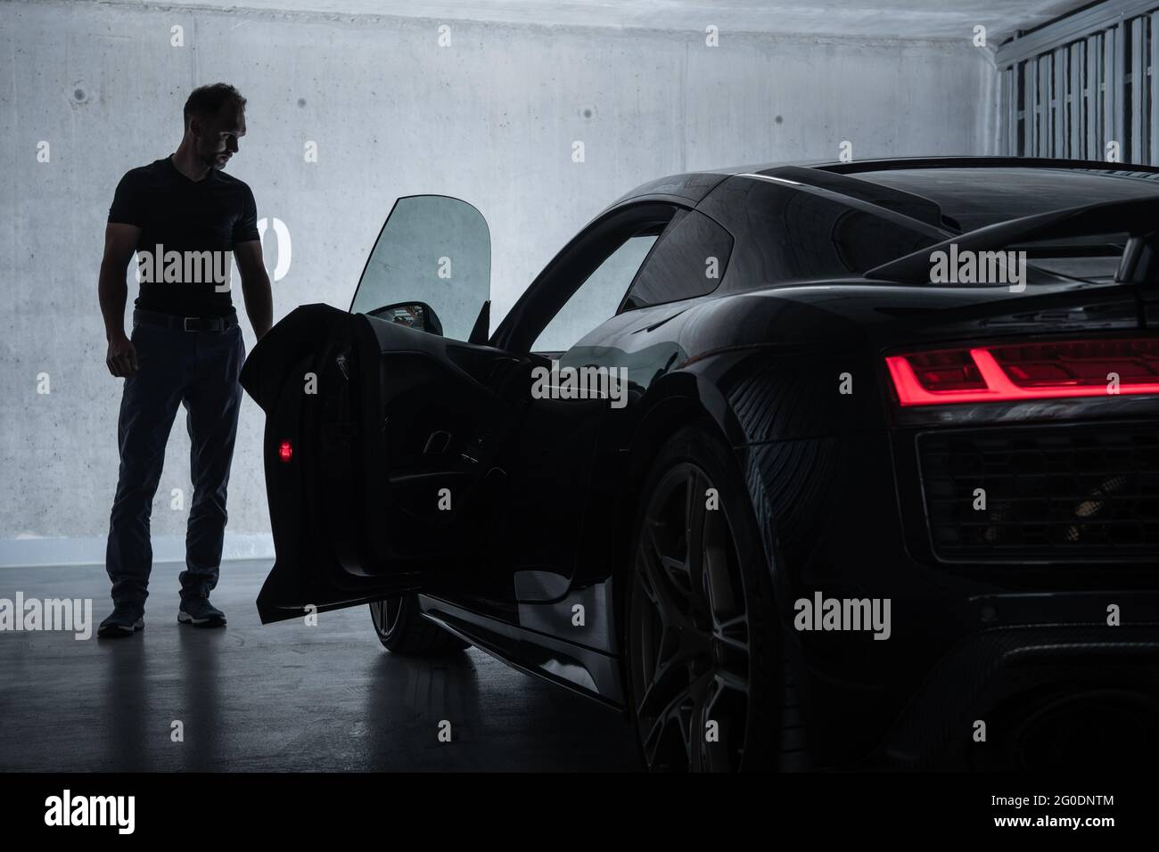 Successful Caucasian Men in His 40s Looking at His Luxury Exotic Car Inside Underground Garage. Car Enthusiast Collection. Stock Photo