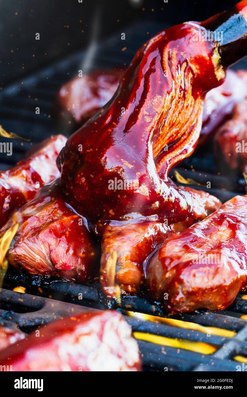 Vertical shot of boneless beef ribs grilling over flames with barbecue sauce added with bbq mop. Extreme shallow depth of field with blurred backgroun Stock Photo