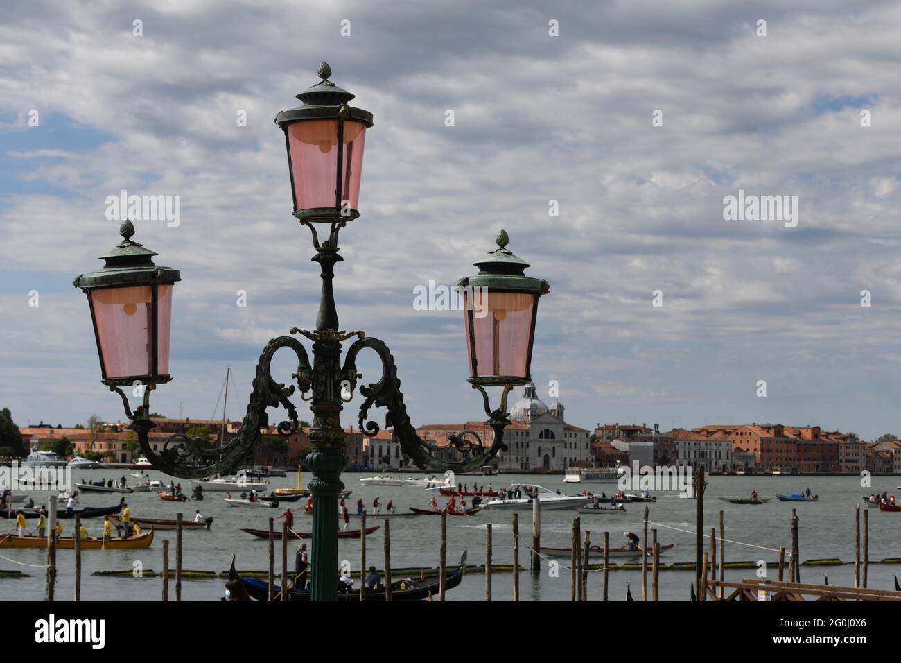 Strassenlaterne am Eingang zum Markusplatz in Venedig gegen den bewölkten Himmel, im Hintergrund eine Regatta am Canale Grande Stock Photo