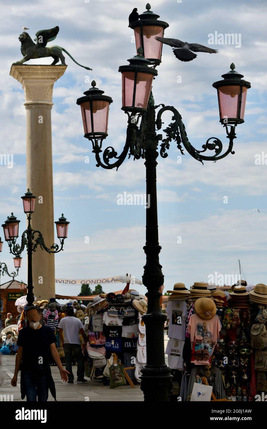Vierarmige Strassenlaterne am Eingang zum Markusplatz in Venedig vor dem Wahrzeichen, dem Markuslöwen, und Verkaufsständen gegen den bewölkten Himmel Stock Photo