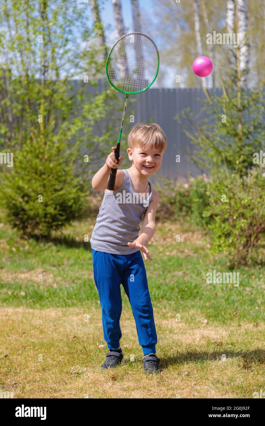 A fair-haired child plays badbinton on the lawn. Stock Photo